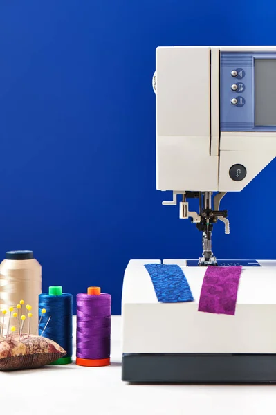 Bobinas de hilos junto a la máquina de coser sobre fondo azul profundo — Foto de Stock
