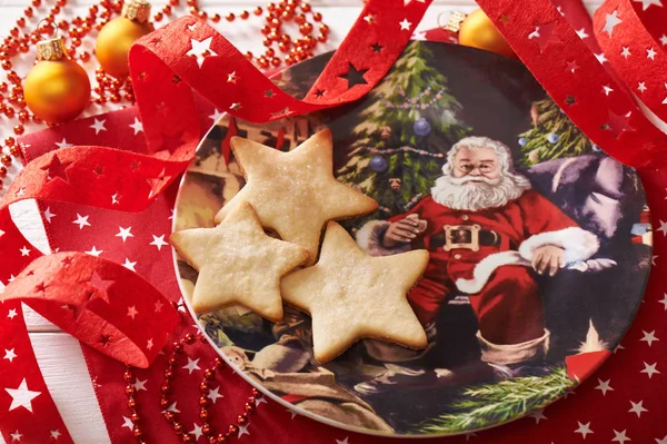 Three cookies in the form of a star on decorative plate surrounded by Christmas decorations — Stock Photo, Image