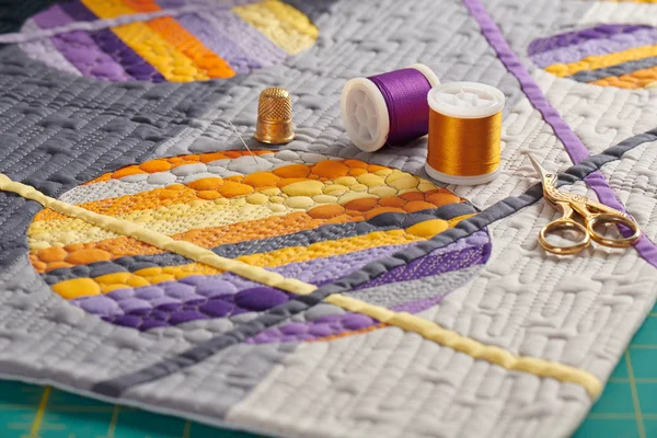 Sewing accessories lying on a mini quilt with orange-purple geometric pattern — Stock Photo, Image