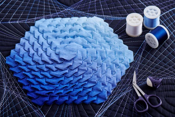 Spoelen van garen, vingerhoedjes, naalden en scharen die op een origami quilt liggen — Stockfoto