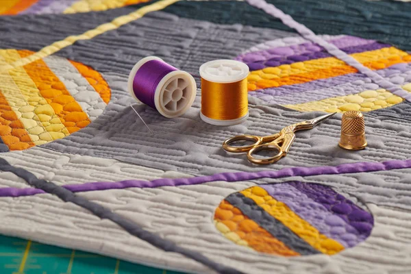 Accessori per cucire adagiati su una mini trapunta con motivo geometrico arancio-viola — Foto Stock