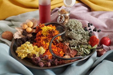 Elle boyanmış kumaşların arka planına karşı organik kumaş boyası yapmak için bitkisel malzemelerle dolu bir tabak.