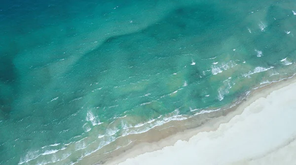Білий пісок біля моря з блакитною водою і пінистими хвилями . Стокове Зображення