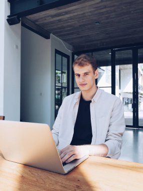 Güneşli bir günde ortak çalışma alanında dizüstü bilgisayarıyla çalışan genç ve güzel bir adam. Dikey fotoğraf.