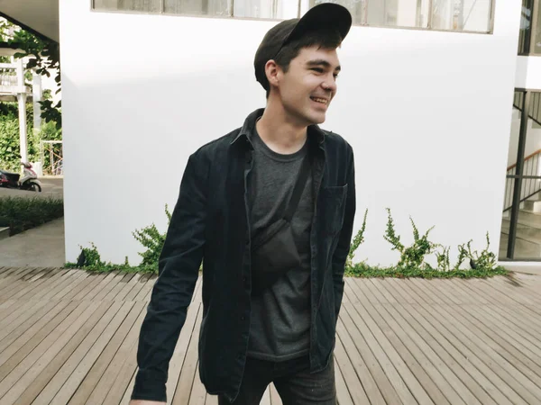 Αστεία αγόρι σε μαύρο καπέλο στη σκιά περπάτημα στην αυλή του ξενοδοχείου λευκό τοίχο στο παρασκήνιο — Φωτογραφία Αρχείου