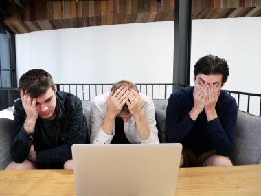 Stressed men freelancers holding hands on faces in working space