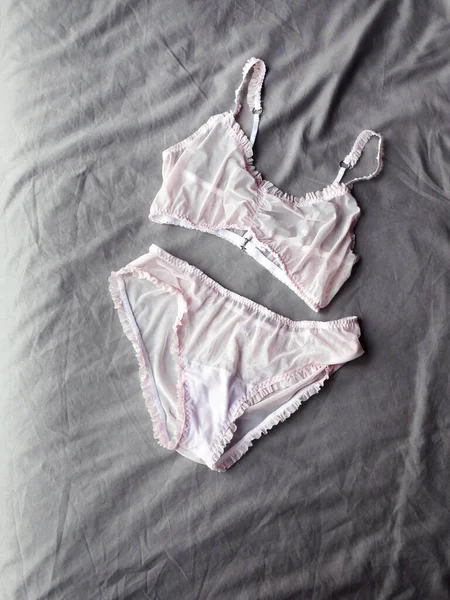 Women's pink gentle sexy lingerie lying at grey bed as background. Vertical photo — 스톡 사진