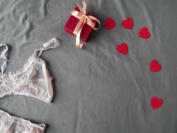 Roupa interior rosa das mulheres e caixa de cintura vermelha na cama cinza como fundo — Fotografia de Stock