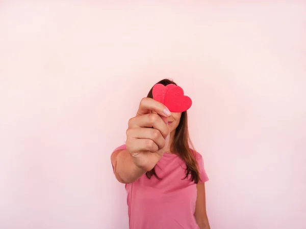 Menina irreconhecível mostra a forma do coração da câmera na parede rosa no fundo. Dia dos namorados — Fotografia de Stock