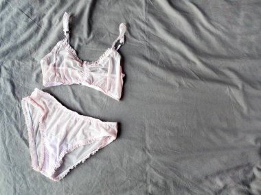 Arka plan olarak gri yatakta uzanan pembe, nazik seksi iç çamaşırları. İç çamaşırı.
