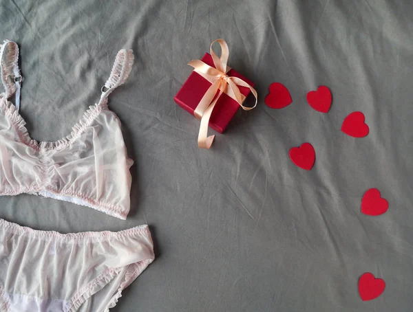 Vista superior de la caja de regalo roja, corazones y ropa interior rosa de las mujeres en la cama gris — Foto de Stock