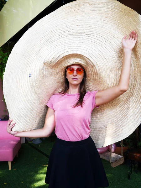 Mulher branca em chapéu de palha gigante em forma de coração óculos de sol e camiseta rosa — Fotografia de Stock