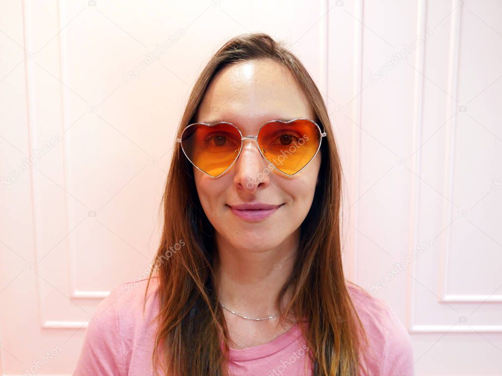 Portrait of young caucasian woman in heart shape sunglasses at pink background