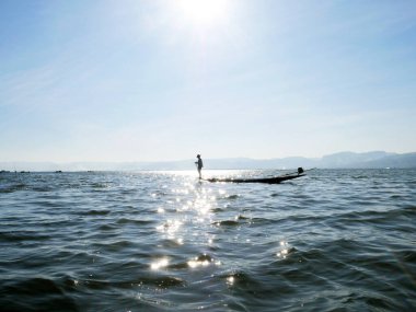 Inle Gölü, Myanmar 24 Şubat 2020 - Güneş ışığında teknenin kenarında duran balıkçı silueti. İnle Gölü, Myanmar