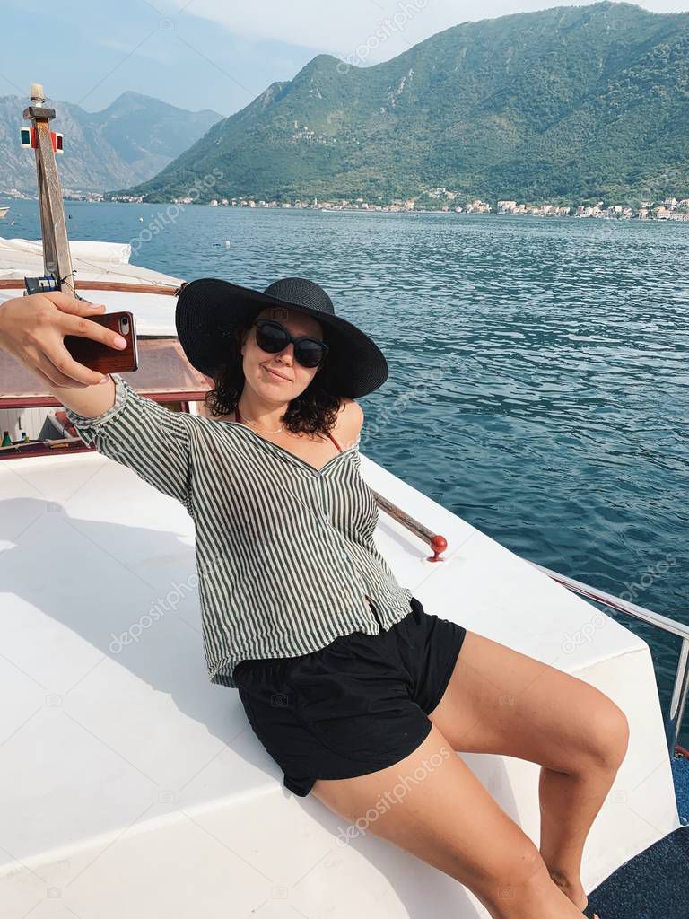 Caucasian woman taking selfie sitting on luxury yacht with amazing beauty landscape at sunny day.
