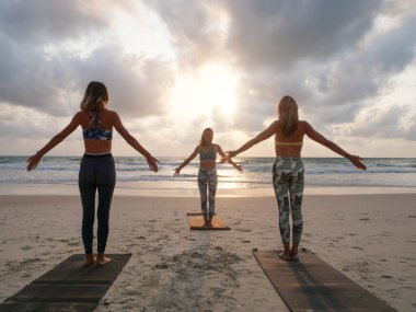 Gün batımında deniz kenarında yoga yapan bir grup kadın..