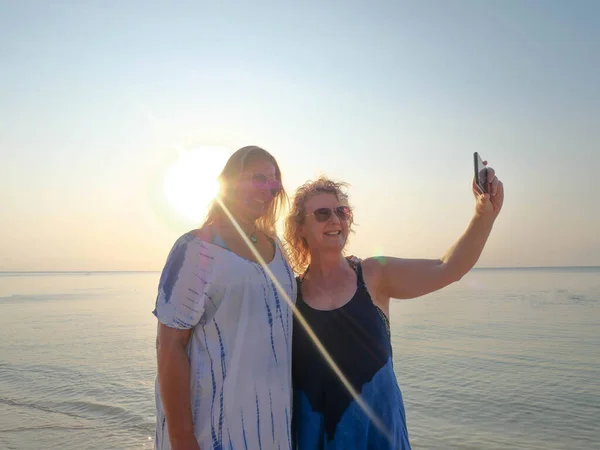 Mulheres idosas felizes fazendo selfie no smartphone na praia do pôr do sol — Fotografia de Stock