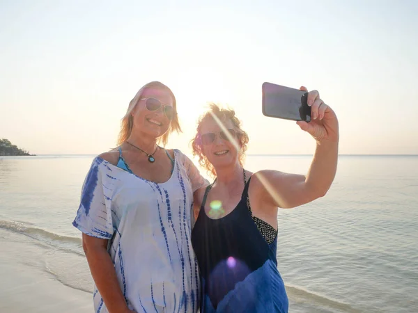 Mulheres idosas felizes fazendo selfie no smartphone na praia do pôr do sol — Fotografia de Stock