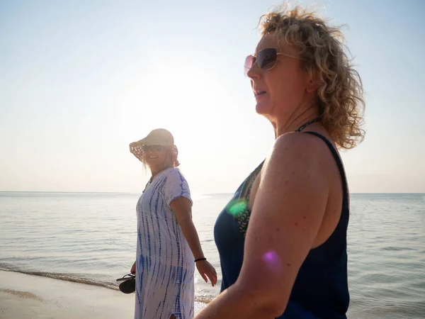 Duas idosas sozinhas em defocus caminham na praia ao pôr do sol — Fotografia de Stock