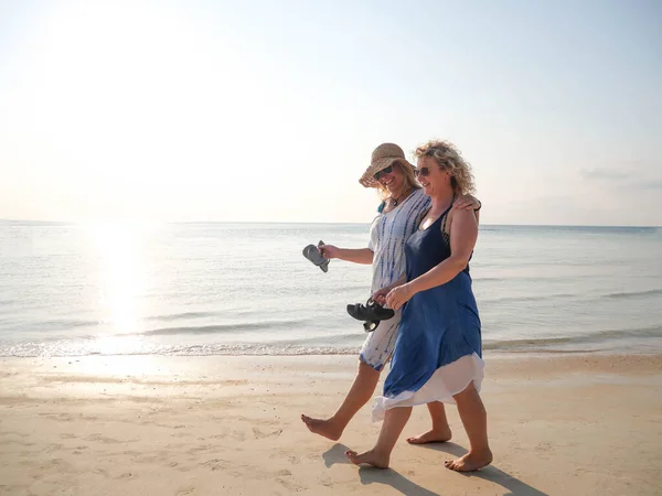 Duas mulheres mais velhas engraçadas andando e rindo na linha costeira no dia ensolarado — Fotografia de Stock