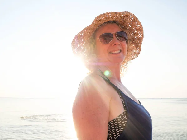 Retrato de mulher mais velha em um chapéu e óculos de sol na praia à luz do sol — Fotografia de Stock