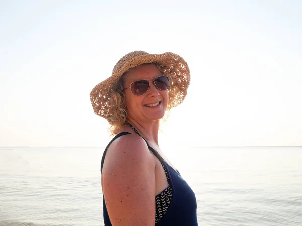 Porträtt av en gammal kvinna i hatt och solglasögon på stranden i solljus — Stockfoto