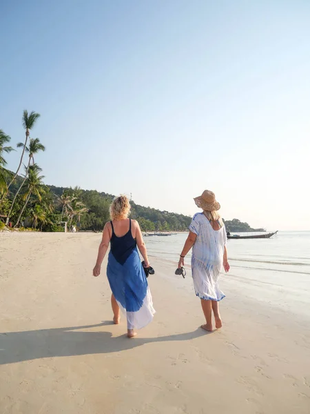 Mulheres idosas andando descalças na costa do mar ao pôr do sol em um país tropical — Fotografia de Stock