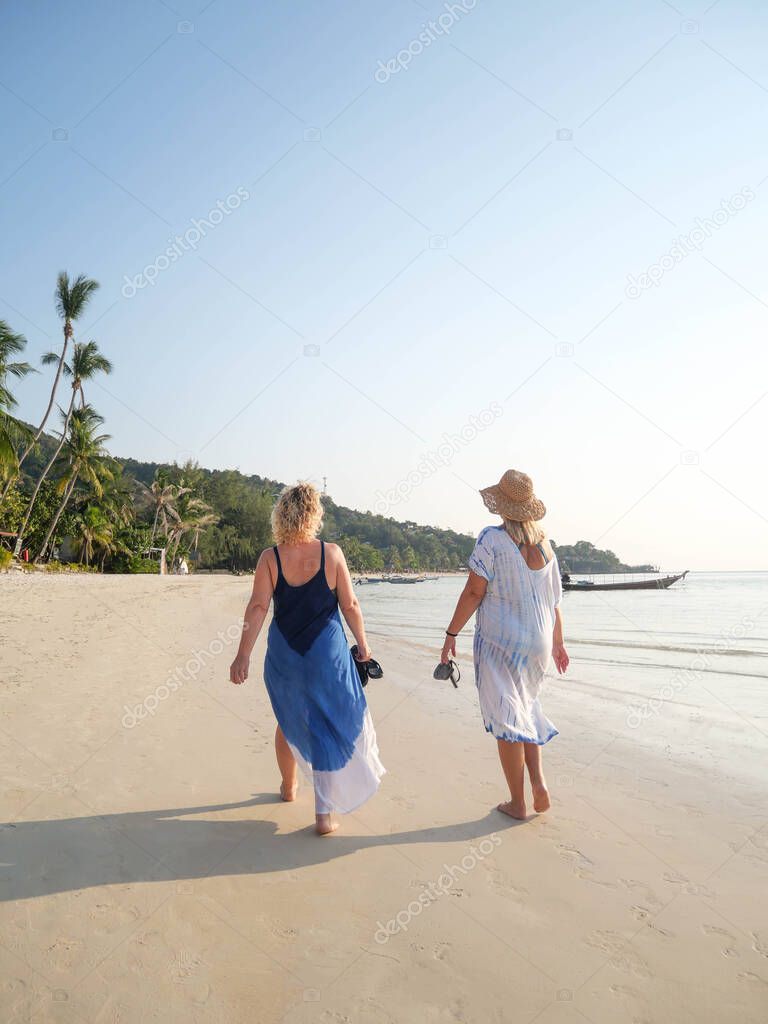 Senior women walking barefoot at sea shore at sunset in tropical country