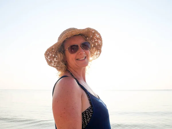 Retrato de mulher sênior em um chapéu e óculos de sol na praia em brilho solar — Fotografia de Stock