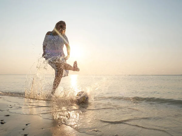 Mulher sênior se divertindo espirrando água e brincando com uma bola no brilho do sol — Fotografia de Stock