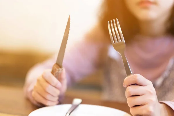 Μια γυναίκα με μαχαίρι μπριζόλας και άδειο λευκό πιάτο στο μπριζολάδικο, μια πεινασμένη γυναίκα που περιμένει φαγητό. — Φωτογραφία Αρχείου