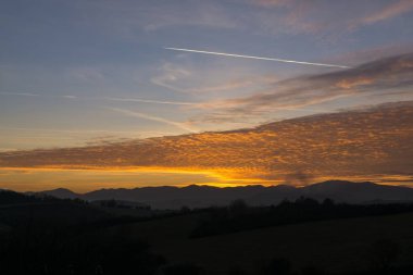 Tepelerin ardında dramatik turuncu gün batımı manzarası