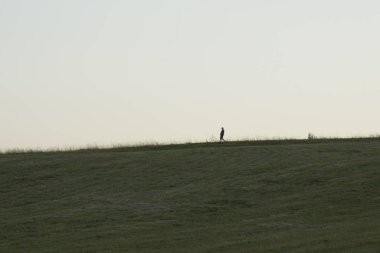 Tepedeki insan silueti, ön planda çimen çimenliği.