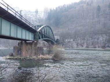 Dağ ormanında nehirden geçen demir köprü.