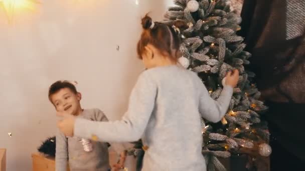 Zwei fröhliche Kinder spielen, wirbeln und lachen am Weihnachtsbaum — Stockvideo