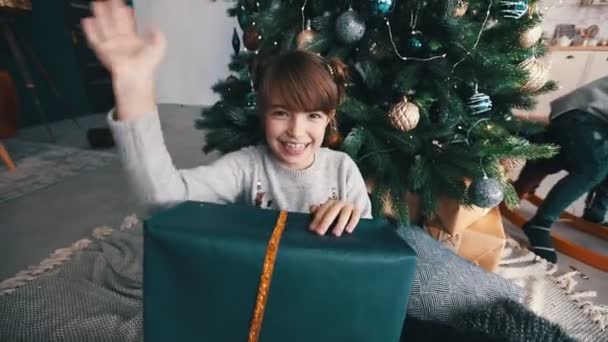 Boldog mosolygós kislány integet kezét a karácsonyfa közelében — Stock videók