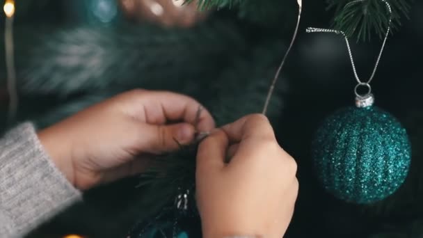 Nahaufnahme von Kinderhänden, die ein Weihnachtsspielzeug an einen Tannenbaum hängen — Stockvideo
