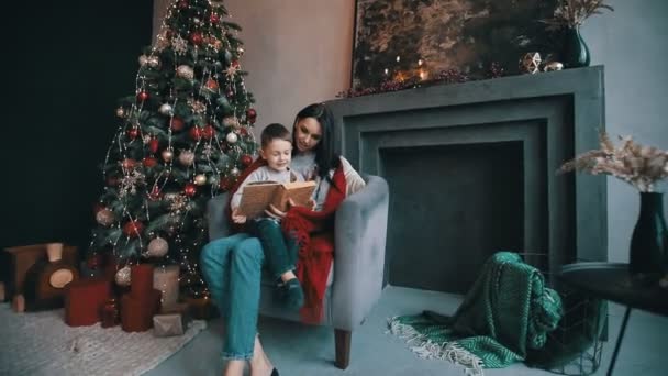 Gyönyörű anya fiával olvas egy mesét közel karácsonyfa
