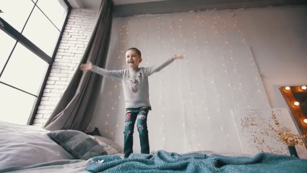 Χαρούμενο και χαμογελαστό αγόρι που πηδάει στο κρεβάτι και πιάνει ένα αρκουδάκι — Αρχείο Βίντεο