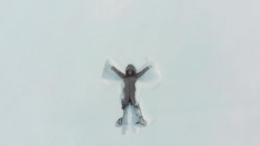 Girl makes snow angel in clearing in the forest