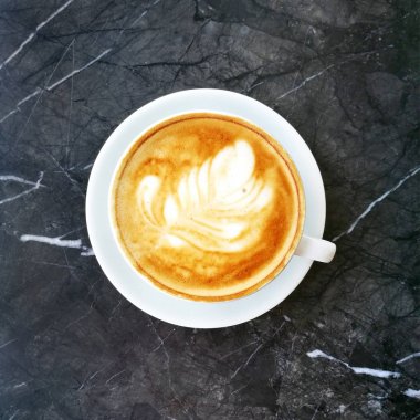 Kahve latte ile yüzey üstten görünüm üzerinde bir tüy. Mermer bir masada kahve fincanı.