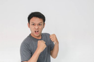 Gri tişörtlü komik Asyalı adam stüdyoda poz veriyor.