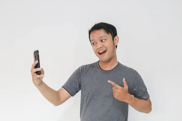 Vtipný Asijský Muž Šedém Tričku Pomocí Smartphonu Gestikulace Při Pózování — Stock fotografie