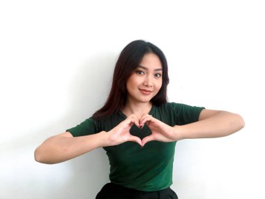 Duygusal Asyalı kız yeşil tişörtlü kalbi gösteriyor.