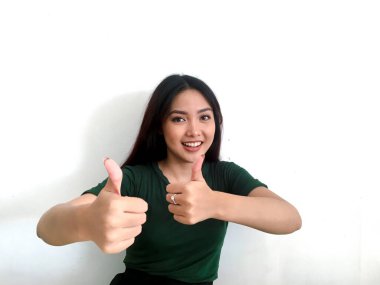 Yeşil tişörtlü gülümseyen Asyalı kız baş parmağını kaldırıyor.