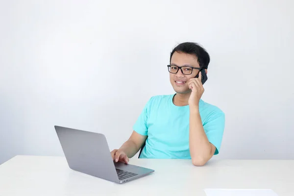 Młody Azjata Szczęśliwą Twarzą Rozmawia Przez Telefon Komórkowy Laptopem Stole — Zdjęcie stockowe