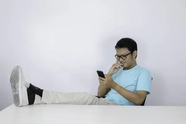 Молодий Азіатський Чоловік Щасливим Обличчям Дивиться Мобільний Телефон Ногою Столі — стокове фото