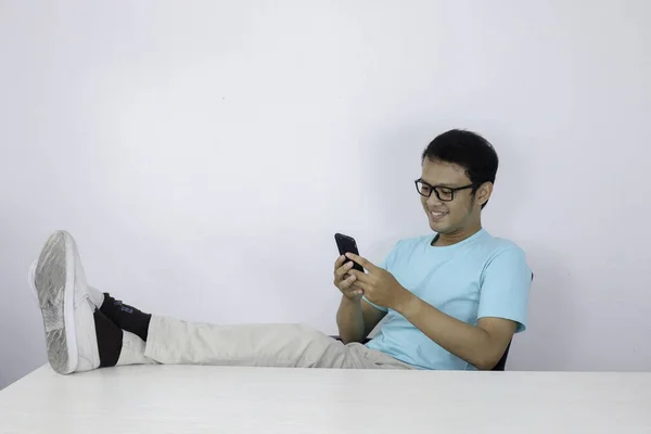 Młody Azjata Szczęśliwą Twarzą Tym Widzi Komórce Nogą Stole Indonezyjczyk — Zdjęcie stockowe