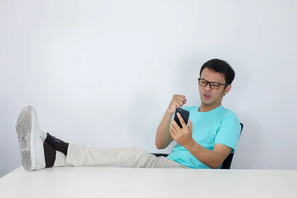 Angry Asian young man get mad when call on the smartphone. Indonesian man wearing blue shirt.