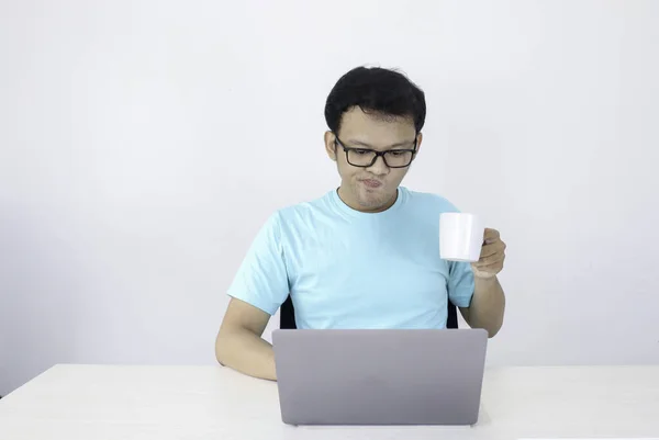 白ガラスのドリンクコーヒーでノートパソコンで働く若いアジア人男性は本気です インドネシア男は青いシャツを着て隔離された灰色の背景 — ストック写真